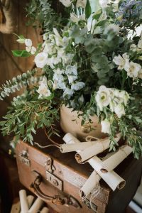 fotografía atrezzo con detalles florales maleta marrón y pergaminos para deco sobre ideas y tendencias en bodas 2022